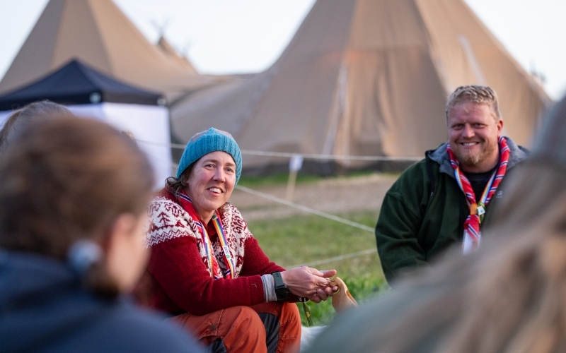 Ledere smiler og sitter samlet og prater med telt i bakgrunnen